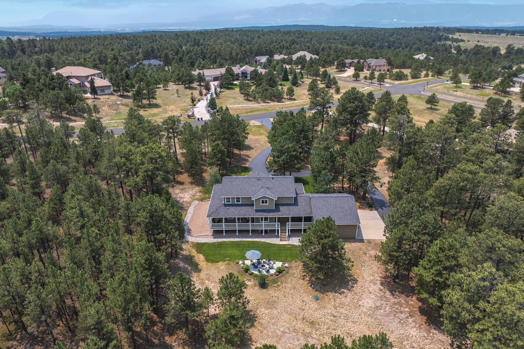 An El Paso County acreage lot seen from above, a house on a treed parcel with a long private drive winding through ponderosa pines.